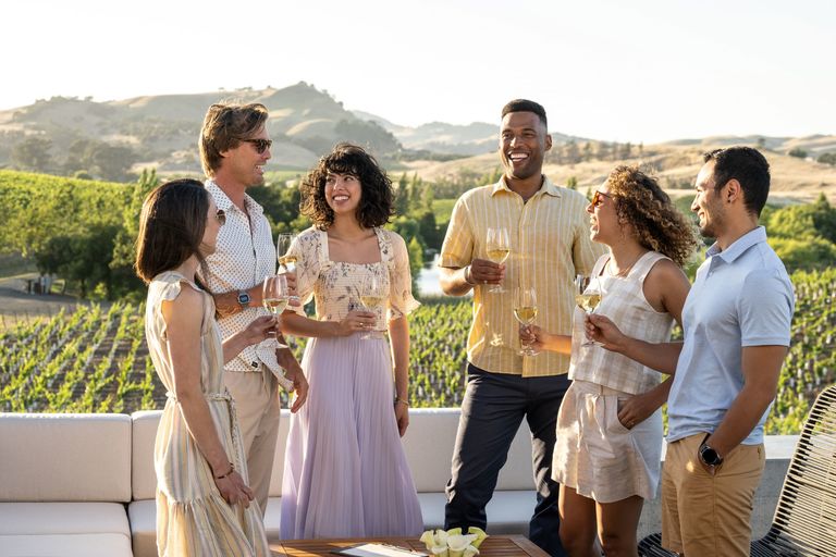 Group of people standing on the patio corner booth, toasting wine glasses and smiling while the sun sets