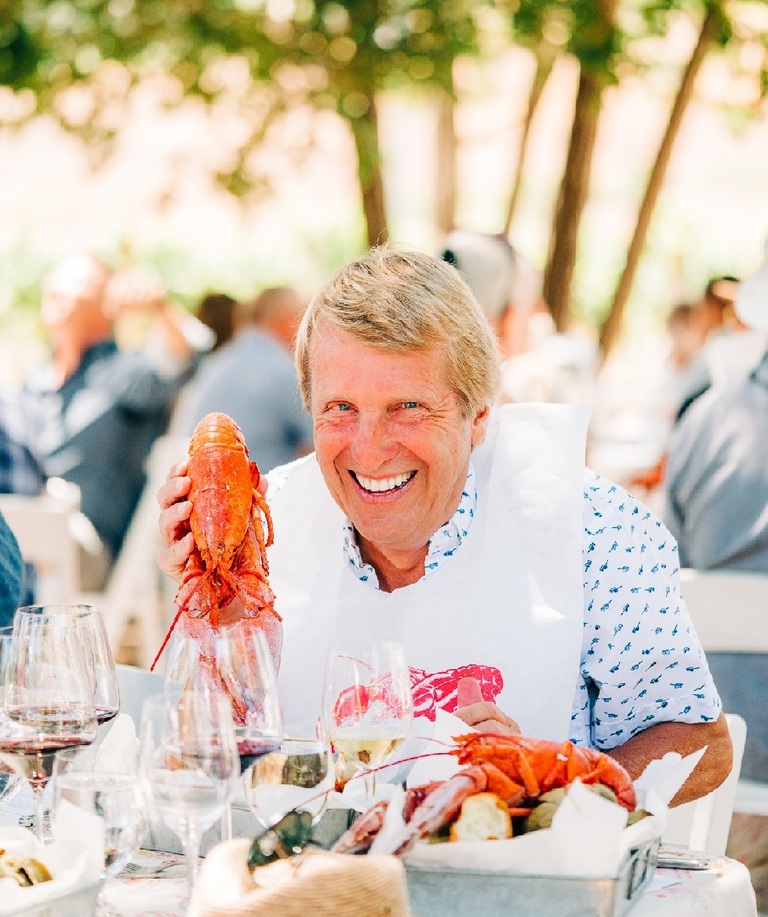 A smiling man holds a cooked lobster