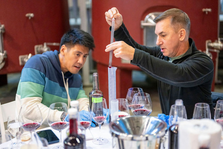 Two men measure beakers of wine