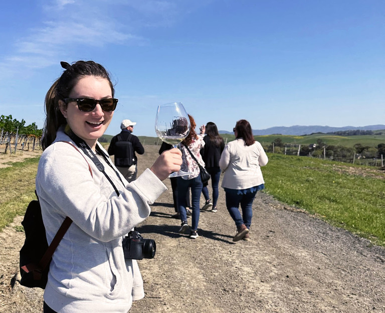 A woman holds a wine glass on a vineyard hike