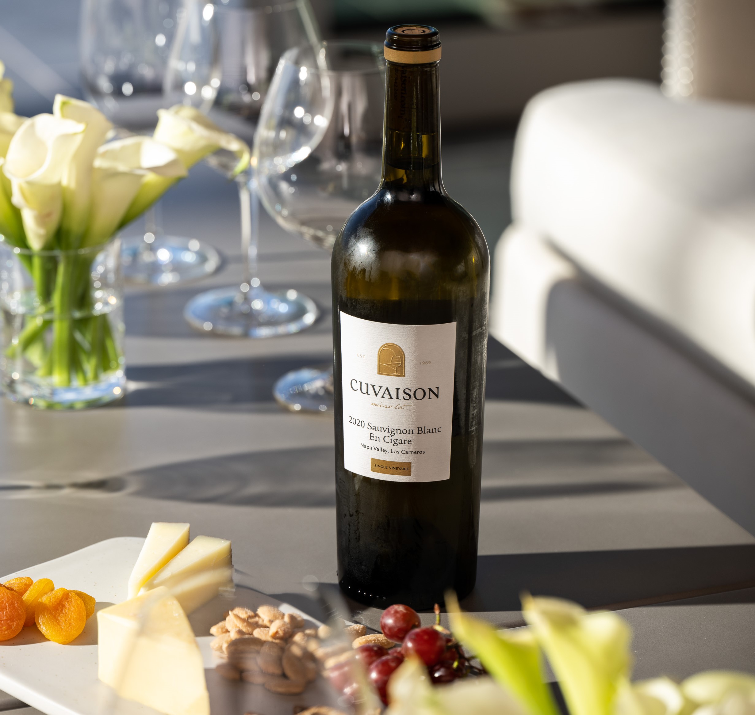 bottle of wine and cheese plate sitting on the table with wine glasses and floral arrangements around