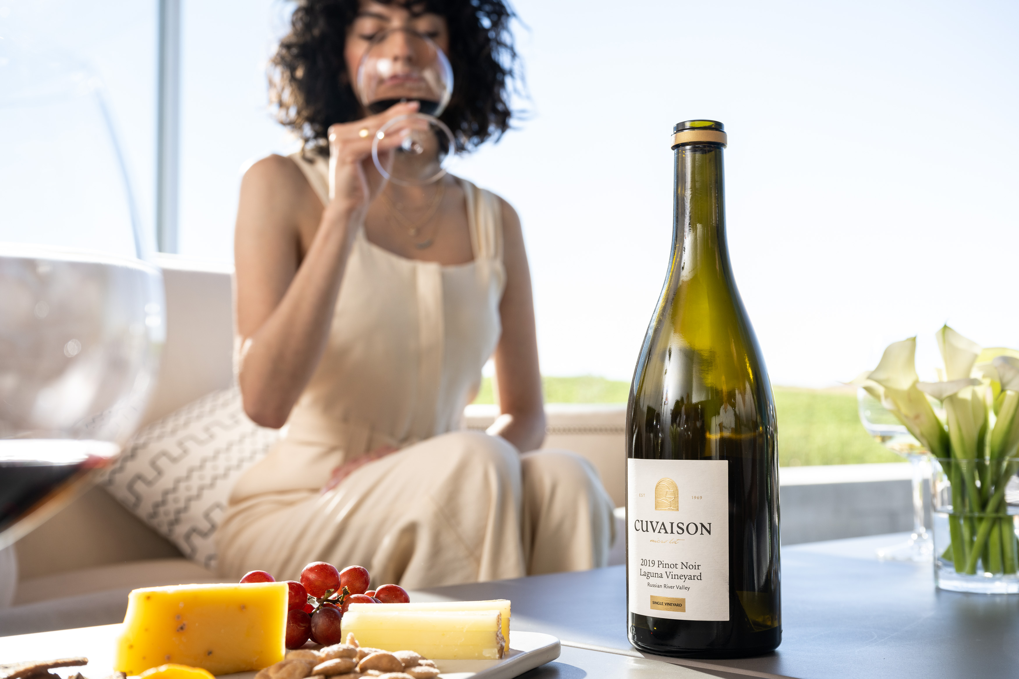 Bottle sitting on table beside cheese plate with woman in the background