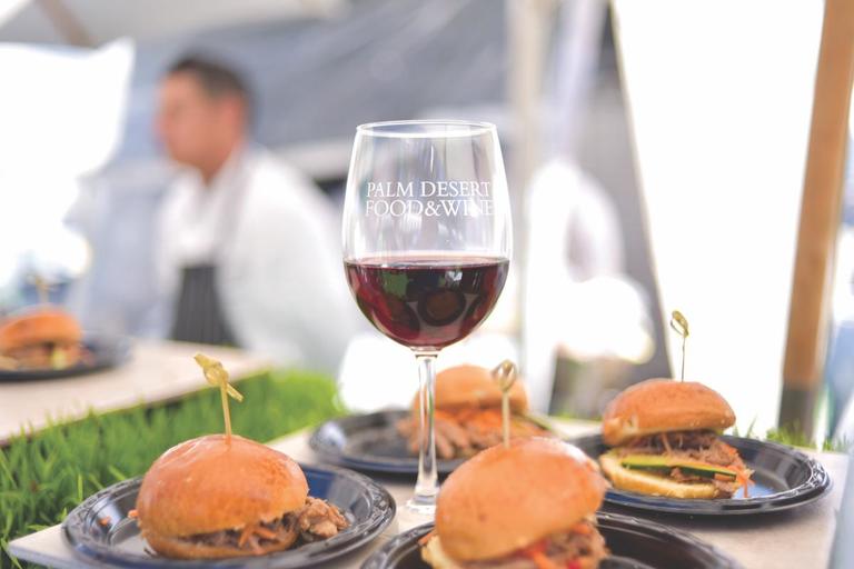 A glass of red wine and a plate of gourmet sandwiches.