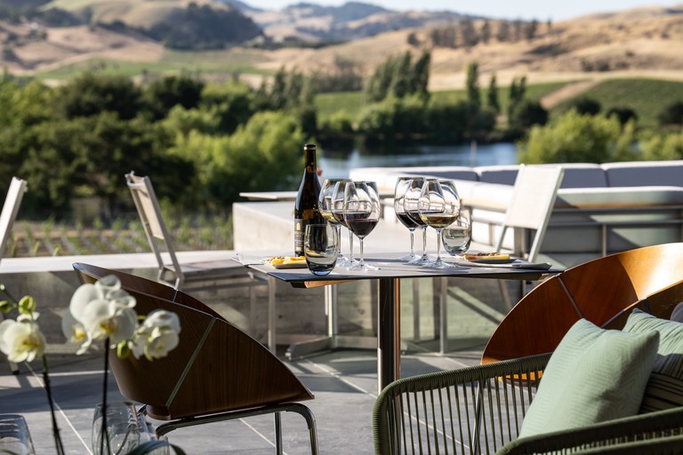 Wine glasses on a table with rolling vineyards in the background.